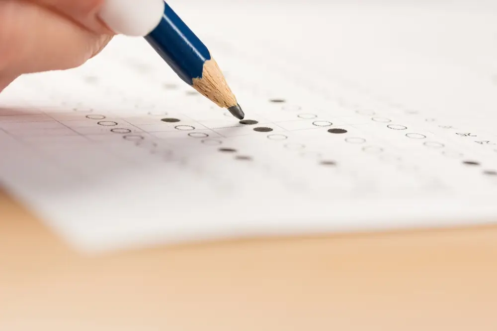 Candidato che compila un test a risposta multipla con una matita durante una prova di concorso.