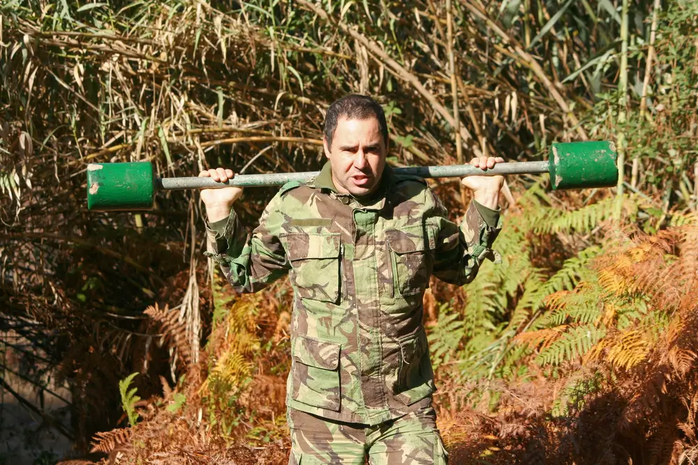 Recluta in divisa mimetica durante un addestramento fisico con un bilanciere all'aperto per il concorso militare.