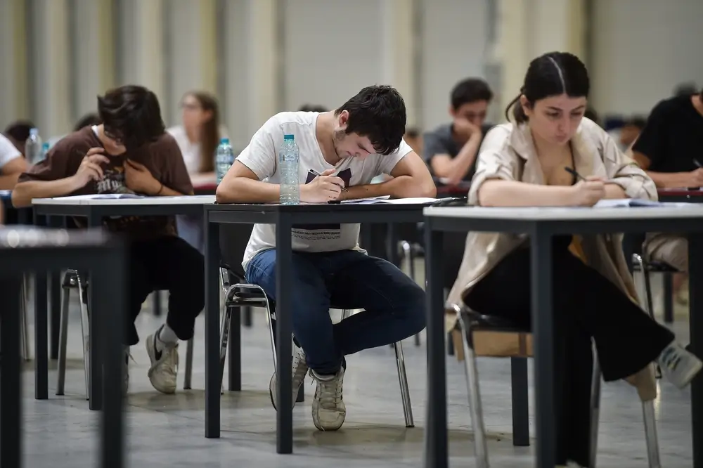 Candidati concentrati durante la prova scritta di un concorso pubblico seduti ai banchi in un'ampia sala d'esame.