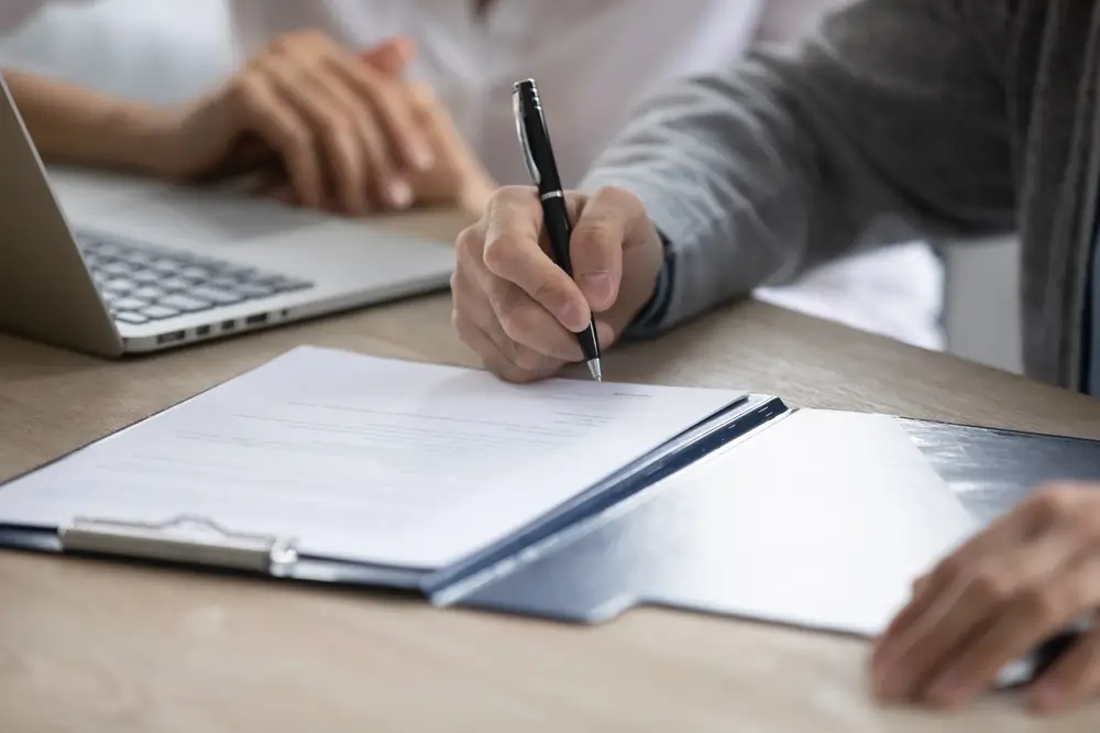 Uomo impegnato nella compilazione di un questionario informativo scrivendo con una penna su un modulo cartaceo.