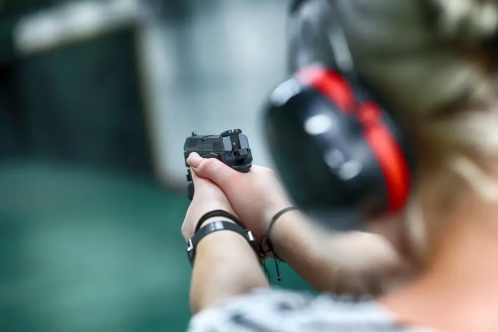 Allievo ispettore in addestramento con equipaggiamento militare mentre mira con una pistola al poligono di tiro.