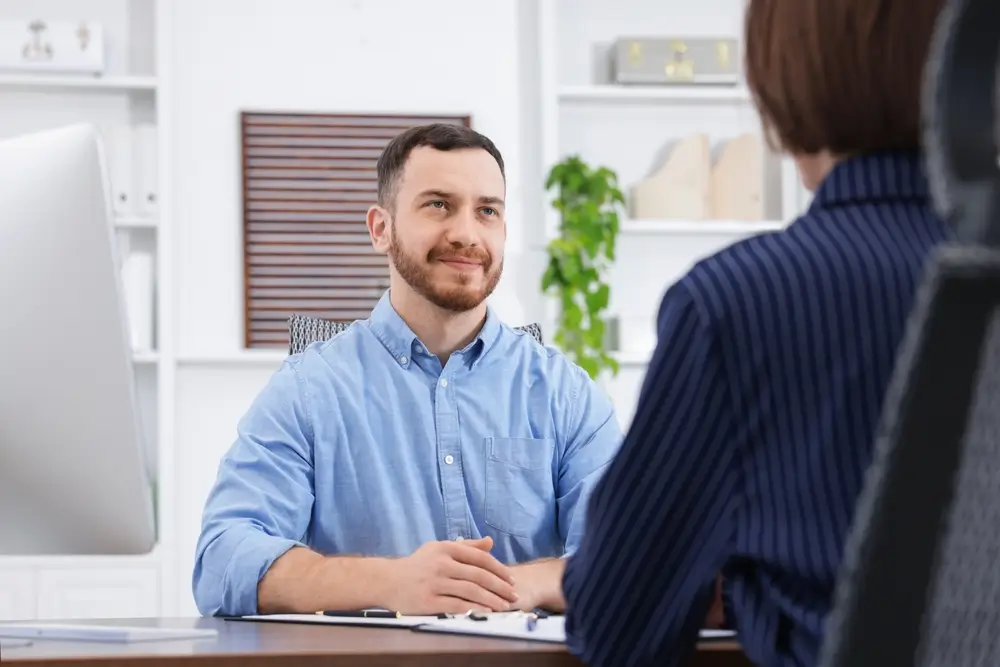 Candidato sorridente durante un colloquio di lavoro e incontro professionale con una selezionatrice in ufficio.