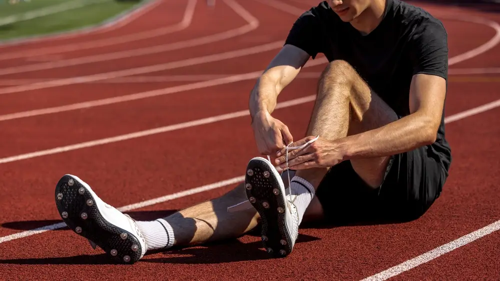 Un atleta si allaccia le scarpe chiodate sulla pista di atletica, preparandosi per le prove fisiche di corsa.