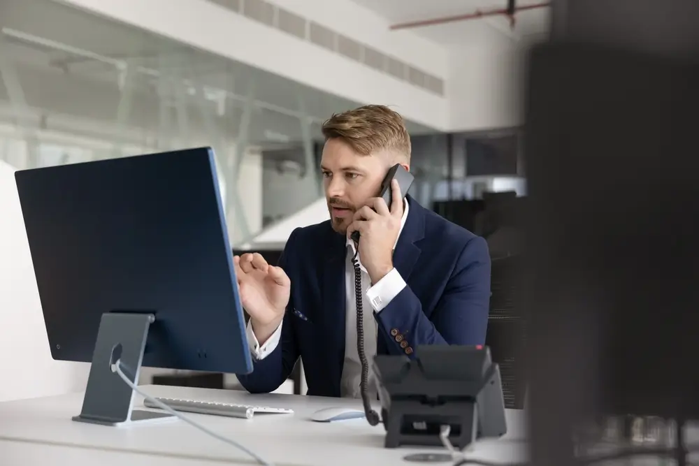 Ufficiale della Guardia di Finanza che coordina le attività d’ufficio parlando al telefono davanti al computer.