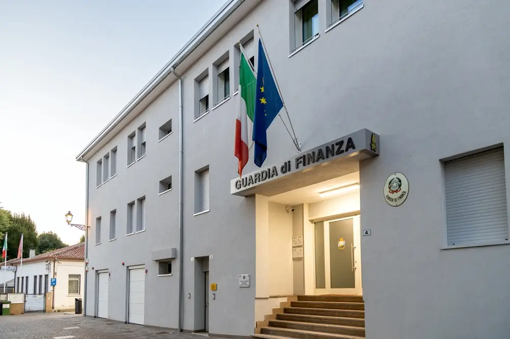 Ingresso della caserma della Guardia di Finanza affacciato sulla piazza, con bandiere italiana ed europea esposte.