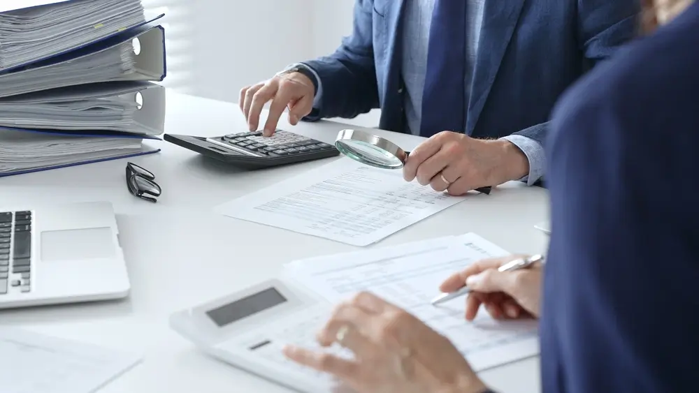 Analisi di documenti contabili in ufficio con lente d'ingrandimento per indagini finanziarie contro il riciclaggio.