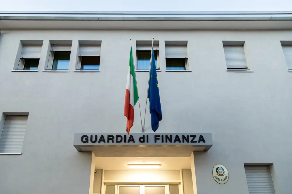 Facciata di una caserma della Guardia di Finanza con insegna ufficiale e bandiere dell'Italia e dell'Unione Europea.